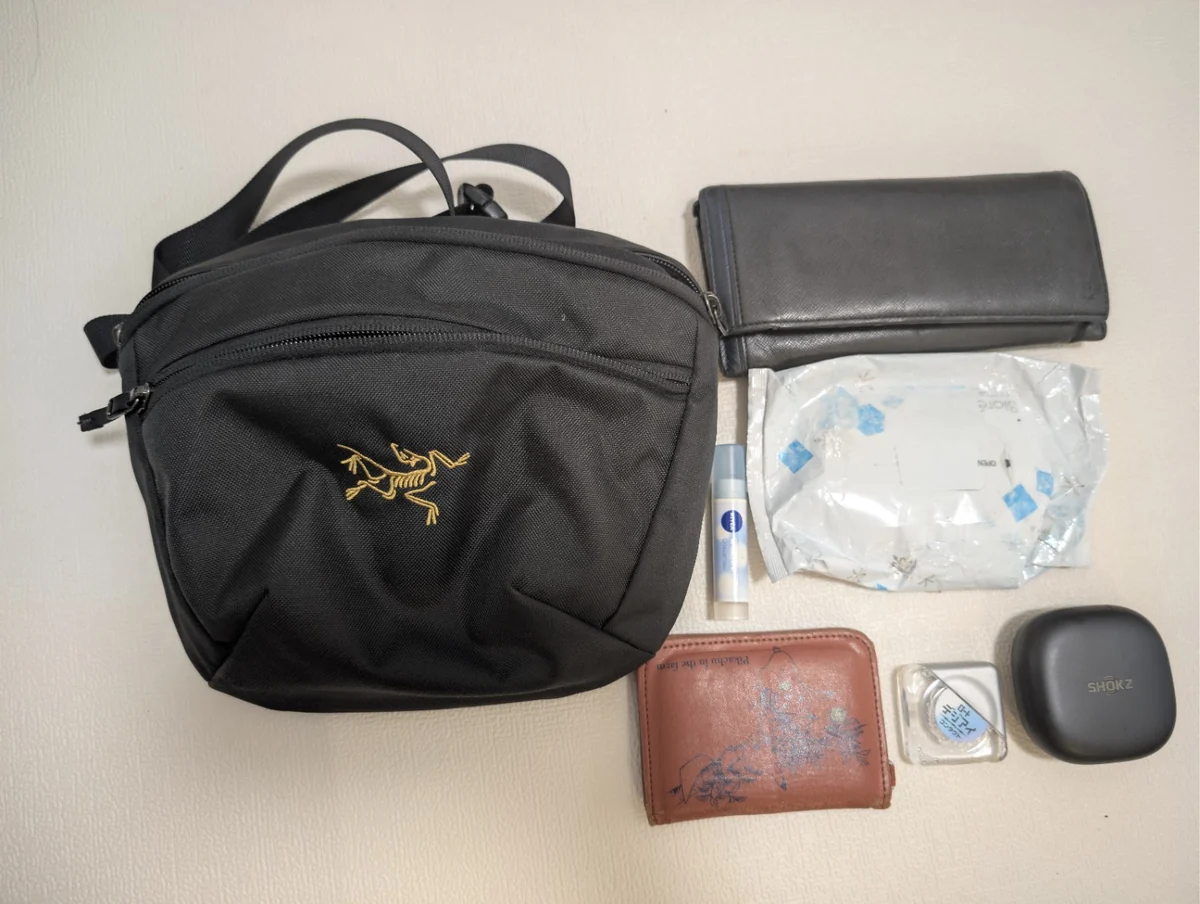 黒いショルダーバッグと長財布、汗拭きシート、リップクリーム、パスケース、目薬、Shokzのケース